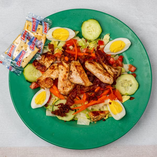 Oakcrest Family Restaurant's grilled chicken salad with bacon, eggs, and crackers on a green plate.