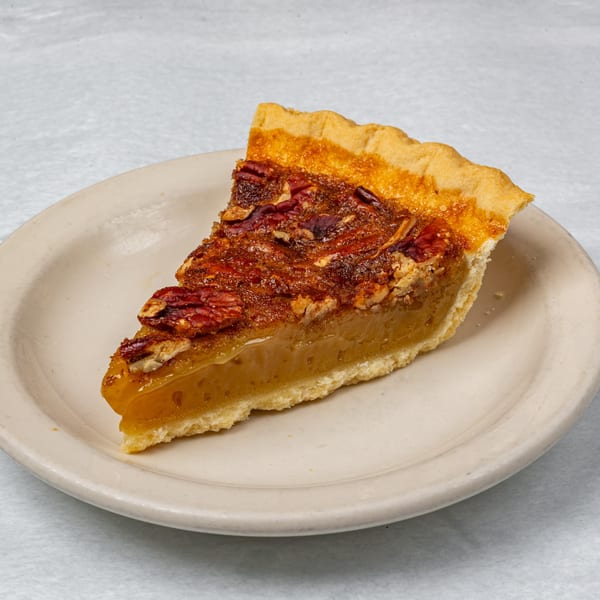 A slice of pecan pie with a golden-brown crust and glistening pecan topping on a white plate.