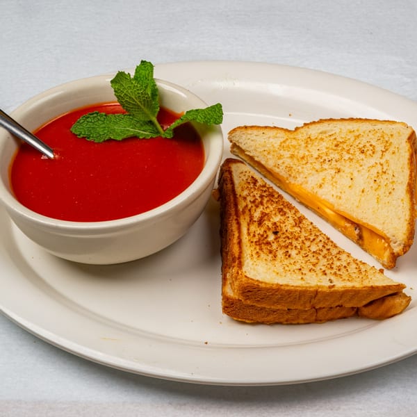 A bowl of tomato soup with a mint garnish and a grilled cheese sandwich cut in half.
