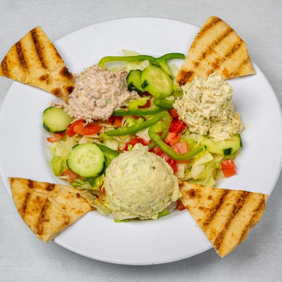 A salad with three scoops of tuna, chicken, and potato salad, surrounded by pita bread.