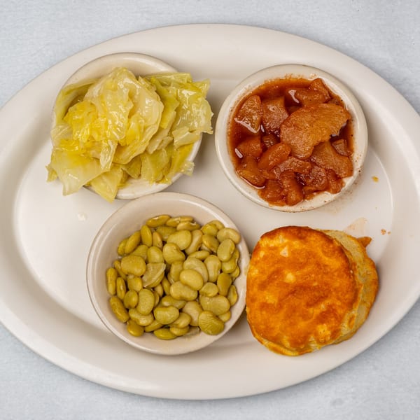 A plate with four small bowls of food: cabbage, stewed apples, lima beans, and a biscuit.