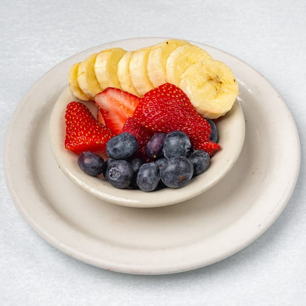 A small bowl of fresh fruit, including sliced bananas, whole strawberries, and blueberries.