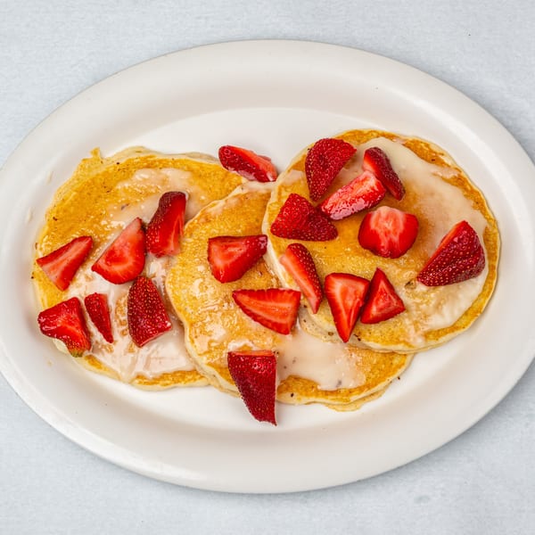 Three golden pancakes topped with white glaze and fresh strawberry slices on a white plate.