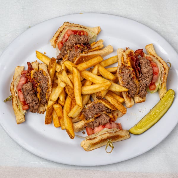 Oakcrest Family Restaurant's burger club sandwich with fries and a pickle spear on a white plate.